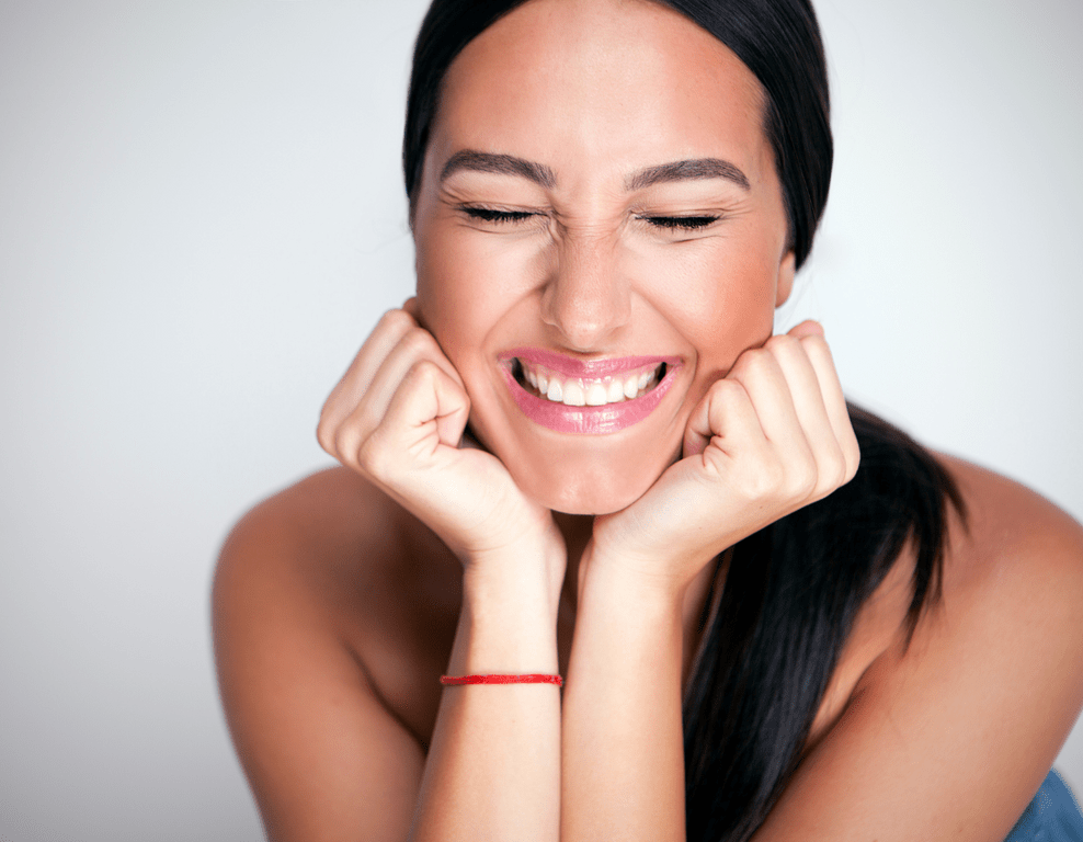 A woman smiling with her hands on her face.